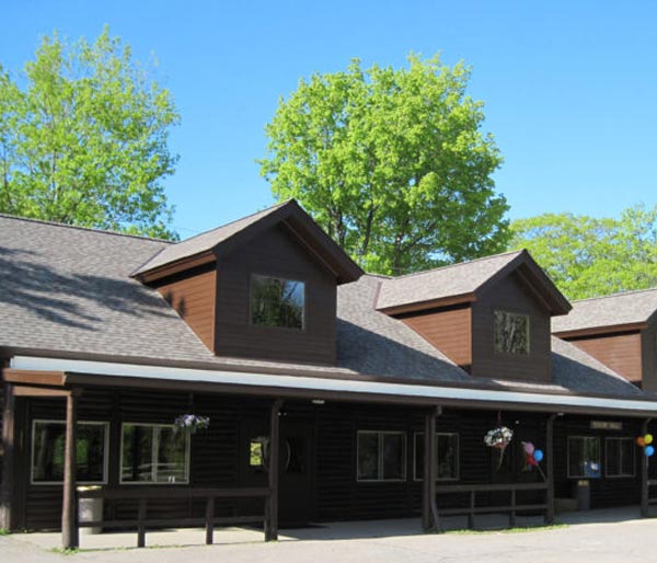 Exterior of a large rustic log cabin building with a covered front porch and dormer windows, known as Taylor Hall.